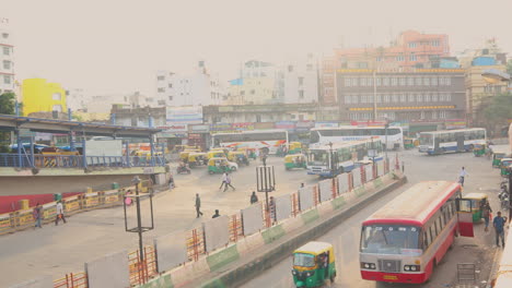 Vista-Aérea-Del-Lapso-De-Tiempo,-Vehículos-Y-Autobuses-De-Transporte-Público-En-El-Círculo-Ocupado-O-Cruce-Cerca-De-La-Estación-De-Autobuses-Urbanos-En-Majestic-Bengaluru,-India