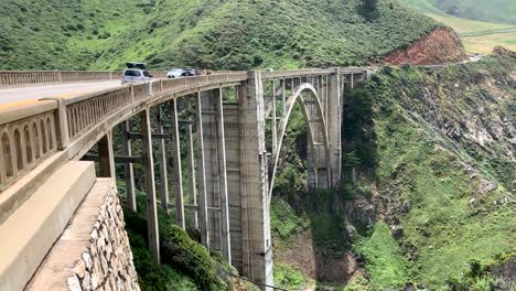 Cars-driving-over-the-Bixby-Creek-Bridge-on-Memorial-Day-weekend-with-breathtaking-views-of-the-lush-green-mountains,-sandy-beaches,-and-aqua-blue-waters-below