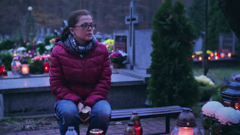 Traurige-Frau-Sitzt-An-Einem-Von-Brennenden-Kerzen-Beleuchteten-Grab