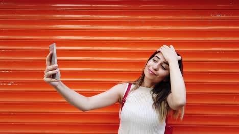 Slow-motion:Beautiful-young-girl-takes-selfie-with-smartphone-in-front-of-orange,red-background