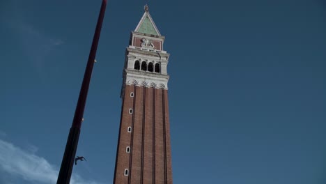 Closeup-of-St-Mark's-Campanile,-blue-sky-background-and-birds-flying-in-Venice,-Italy