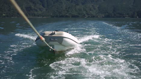 SLOWMO---Inflatable-dinghy-being-towed-on-rope-behind-boat-on-ocean-of-New-Zealand