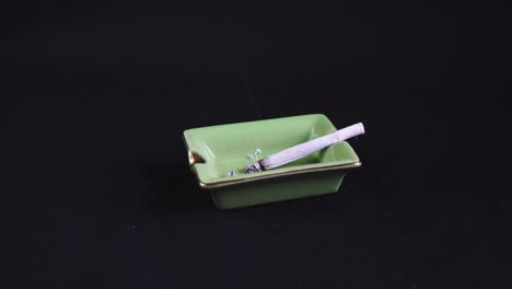 Rolled-Cigarette-or-Joint-burning-out,-legalised-marijuana-on-green-Ashtray