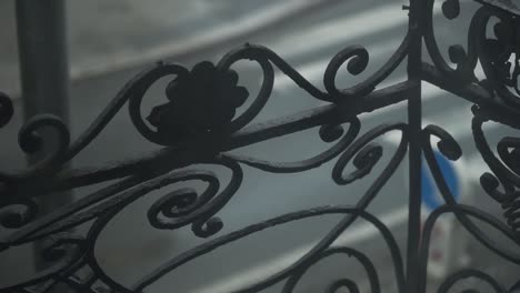 Old-school-metal-balcony-railing-with-decoration---spirals-and-leaves,-cars-in-a-background