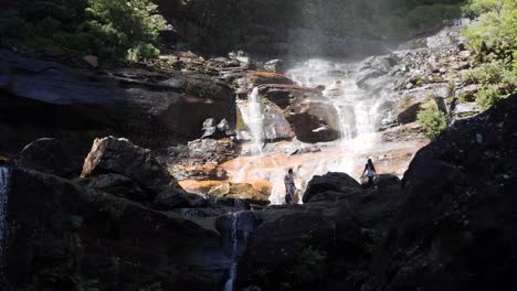 People-walking-and-enjoying-a-rock-pool-at-the-bottom-of-a-waterfall-during-a-sunny-day-with-high-contrast