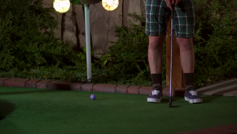 A-close-up-of-a-purple-mini-golf-ball-getting-hit-with-a-club-and-the-shot-is-horrible-and-the-ball-comes-rolling-back-to-the-golfer