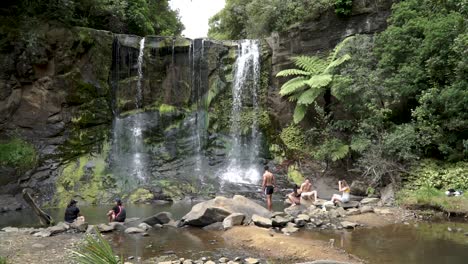 Group-of-young-people-sitting-by-Mokora-Falls,-Auckland,-New-Zealand