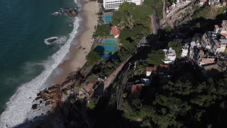 Top-down-aerial-view-on-Vidigal-beach-with-the-ocean-waves-coming-in-showing-the-swimming-pools-and-tennis-courts-next-to-a-hotel