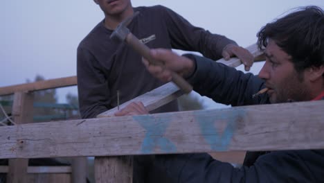 Afghan-refugee-constructs-makeshift-shelter-at-dusk-hammering-nail-into-pallet-wood