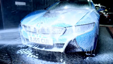 Professional-Worker-Spraying-Shampoo-Foam-at-the-Front-of-a-Blue-luxury-Car-during-a-professional-car-wash