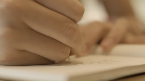 Close-Up-Of-Hand-Holding-A-Pen-And-Writing-On-A-Notebook