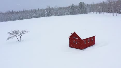 Orbiting-around-a-red-barn-and-an-apple-tree-in-a-snowy-field-during-a-blizzard-SLOW-MOTION-AERIAL