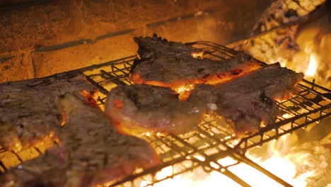 Barbecuing-sizzling-beef-steaks-on-open-fire,-flames-licking-meat-a-fat-drips-on-coals