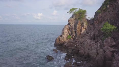 Aerial:-flying-over-a-rocky-hill-near-the-ocean,with-a-single-green-tree-on-top-of-it,-Chantaburi-province,-Thailand