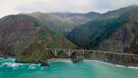 Aerial-shot-of-a-car-driving-over-Bixby-Creek-Bridge-in-Big-Sur-on-State-Route-1-in-California