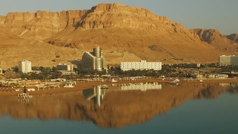 Beach-Resort-Reflected-by-the-Dead-Sea-with-a-huge-mountain-desert-behind