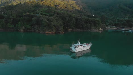 SLOWMO---Morning-aerial-flying-around-cruise-boat-anchored-in-bay-in-Marlborough-Sounds,-New-Zealand