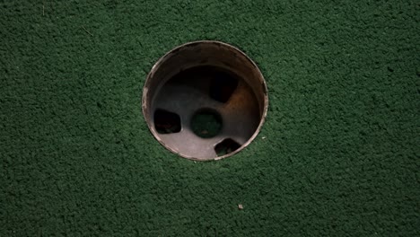 Eine-Nahaufnahme-Eines-Orangefarbenen-Minigolfballs-Aus-Der-Vogelperspektive-Verfehlt-Das-Loch-Auf-Einem-Golfplatz