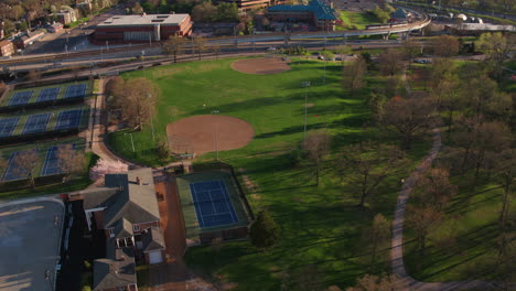 Drone-flies-over-city-park-with-baseball-diamonds-and-tennis-courts