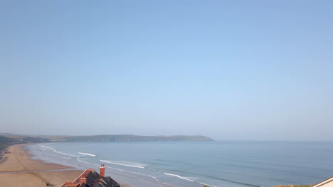 Wellen-Schlagen-Gegen-Einen-Langen-Sandstrand-In-Devon-Und-Verblassen-In-Zeitlupe-Zum-Blauen-Himmel