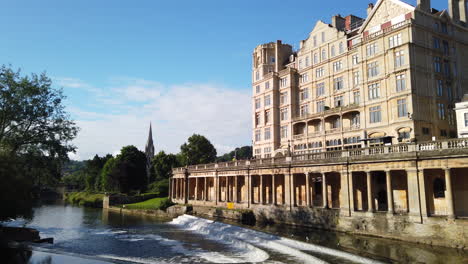 Pulteney-Weir-and-the-Empire-Hotel-in-Bath,-Somerset-on-a-Beautiful-Summer’s-Morning-fading-out-diagonally-to-Clear-Blue-Sky-with-Seagull-Flying-Across-Frame-in-Slow-Motion
