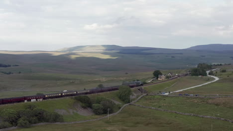 Aerial-Flyaway-Shot-of-the-Flying-Scotsman-60103-Steam-Train-as-it-Passes-Through-Ribblehead-Station-in-North-Yorkshire-with-Narrow-Crop