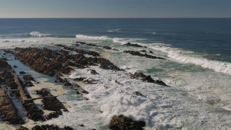 View-from-high-vantage-point-of-rocky-coastline-with-waves-breaking-at-The-Point-of-Mosselbay,-South-Africa