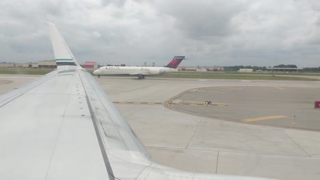 Looking-out-the-window-of-an-airplane-taxiing-at-DTW-Detroit-Metro,-overlooking-the-wing,-cloudy