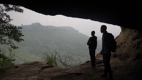 Die-Silhouette-Zweier-Afrikanischer-Männer-Und-Eines-Hundes-Aus-Einer-Höhle-Mit-Blick-Auf-Ein-Afrikanisches-Tal