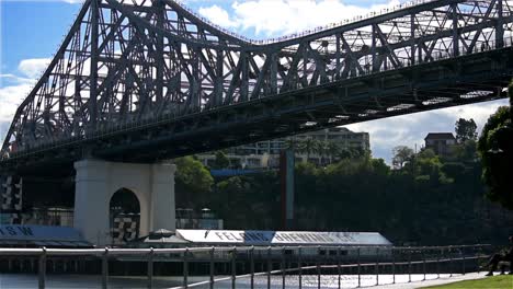 Jogger-Laufen-Am-Ufer-Des-Sonnendurchfluteten-Brisbane-River-Am-Kangaroo-Point-Entlang,-Hoch-Oben-Ragt-Die-Berühmte-Story-Bridge-Empor