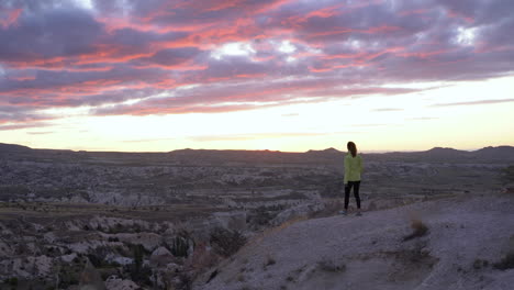 Woman-walking-to-the-cliffs-edge-to-admire-the-sunset-at-Red-Valley-in-Goreme,-Turkey