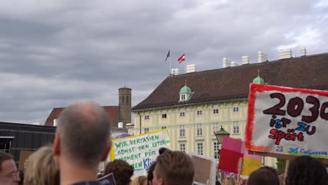 View-of-crowd-holding-up-signs-with-backdrop-of-Austrian-and-European-flag-during-fridays-for-future-climate-change-protests