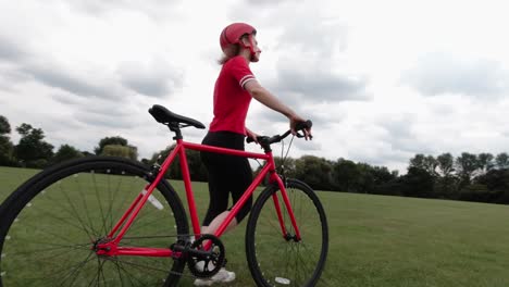 Caucasian-female-cyclist-in-red-top-walking-with-her-bike-in-a-park