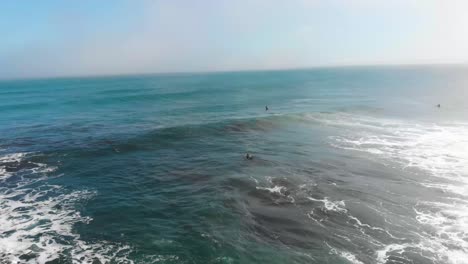 Aerial-Cinematic-shot-of-waves-and-Surfers-Swimming-on-a-sunny-day-in-Pichilemu,-Chile-4K