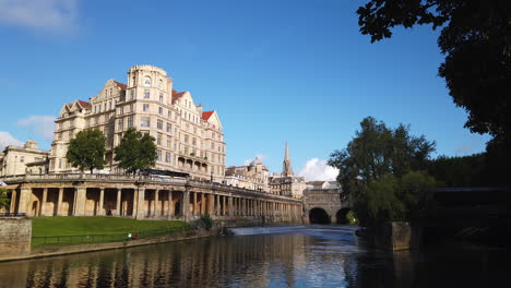 Time-Lapse-of-the-Empire-Hotel,-Pulteney-Weir---Pulteney-Bridge-in-Bath,-Somerset-on-Beautiful-Summer’s-Morning-with-Blue-Sky-and-Golden-Light
