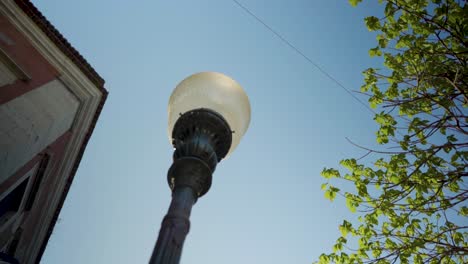 Old-city-street-tilt-up-to-street-lamp-bulb-with-blue-sky-and-green-leaves