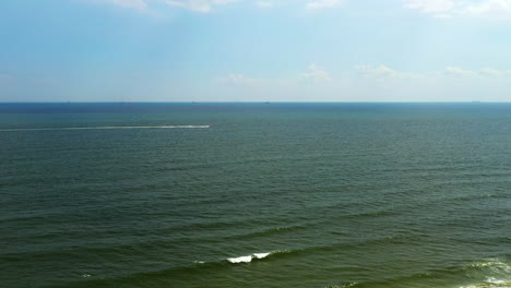 aerial-shot-over-the-ocean-in-Long-Beach,-New-York-as-a-fast-boat-moves-off-in-the-distance-towards-the-right