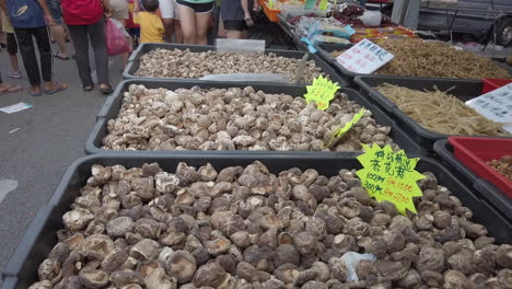 Variety-display-of-dried-fungus-mushrooms-along-the-street-with-people,-price-tag-and-plastic-bags-in-the-background