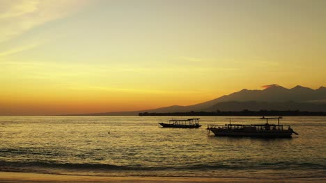 Goldene-Stunde-Der-Dämmerung-Mit-Gelbem,-Staubigem-Himmel-über-Der-Silhouette-Von-Bergen-Und-Ruhiger,-Dunkler-Lagune-Mit-Schwimmenden-Fischerbooten-In-Indonesien