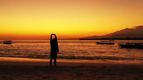 Girl-with-outstretched-hands-admiring-majestic-golden-sunset-over-the-tropical-sandy-beach