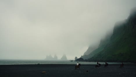 Horses-running-in-SlowMotion-across-black-sand-beach,-in-a-foggy-day-in-Vik,-Iceland