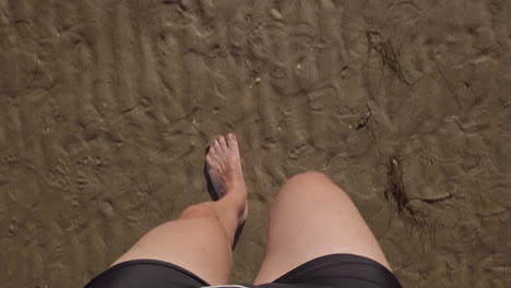 POV-First-person-view-of-a-man-walking-on-wet-sand,-black-bathing-suit