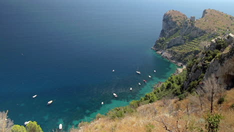 Rocky-Coastline-And-Turquoise-Sea-Surface-With-Boats-Moored-In-Amalfi-Coast