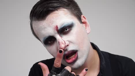 Face-painted-man-showing-tongue-and-devil-horns-fingers,-closeup-portrait,-slowmo
