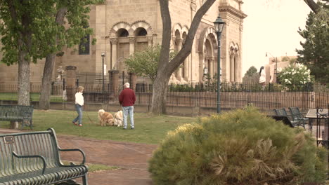 Retired-couple-walks-their-dogs-in-the-courtyard-next-to-an-old-church-building-still-shot