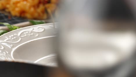 Close-up-shot-made-on-motorized-slider-from-left-to-right-through-glass-bottle,-taking-fusilli-pasta-from-pan-using-plastic-spatula-and-placing-it-on-white-deep-plate