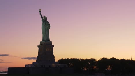 Einspielaufnahme-Der-Silouhette-Der-Freiheitsstatue-Im-Morgengrauen,-Aufgenommen-Von-Einem-Boot-Aus-Auf-Orange-violettem-Hintergrund