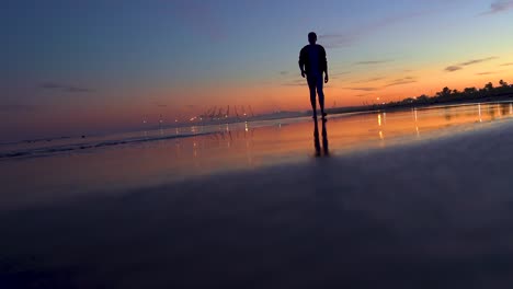 Mann-Läuft-Bei-Sonnenuntergang-Barfuß-Auf-Dem-Sand-An-Einem-Wunderschönen-Strand,-Seine-Fußabdrücke-Auf-Dem-Nassen-Sand-Und-Das-Stehende-Wasser-Der-Meereswellen-Im-Gegenlicht