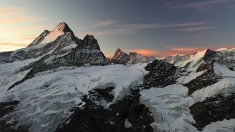 Drohnenaufnahme,-Die-Von-Rechts-Nach-Links-über-Die-Schneebedeckten-Berggipfel-In-Den-Schweizer-Alpen-Schwenkt,-Während-Eines-Farbenfrohen-Und-Dramatischen-Sonnenaufgangs-Mit-Rot-Und-Orange-Gefülltem-Himmel