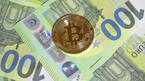 Mano-Masculina-Colocando-Un-Solo-Bitcoin-Dorado-En-Una-Pila-De-Billetes-De-Cien-Euros